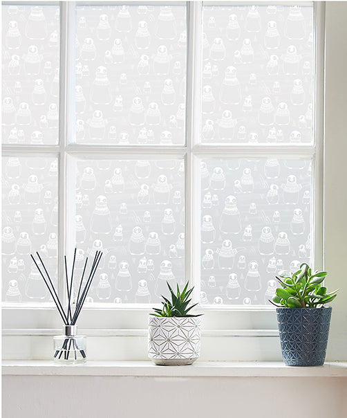 Window with white frames and potted plants on the windowsill, with penguin design printed frosted window film by Helen Russell on the glass. 