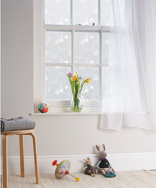 Children's toys on the floor in front of a window with a vase of flowers on the windowsill and Helen Russell white printed window film applied to the glass.