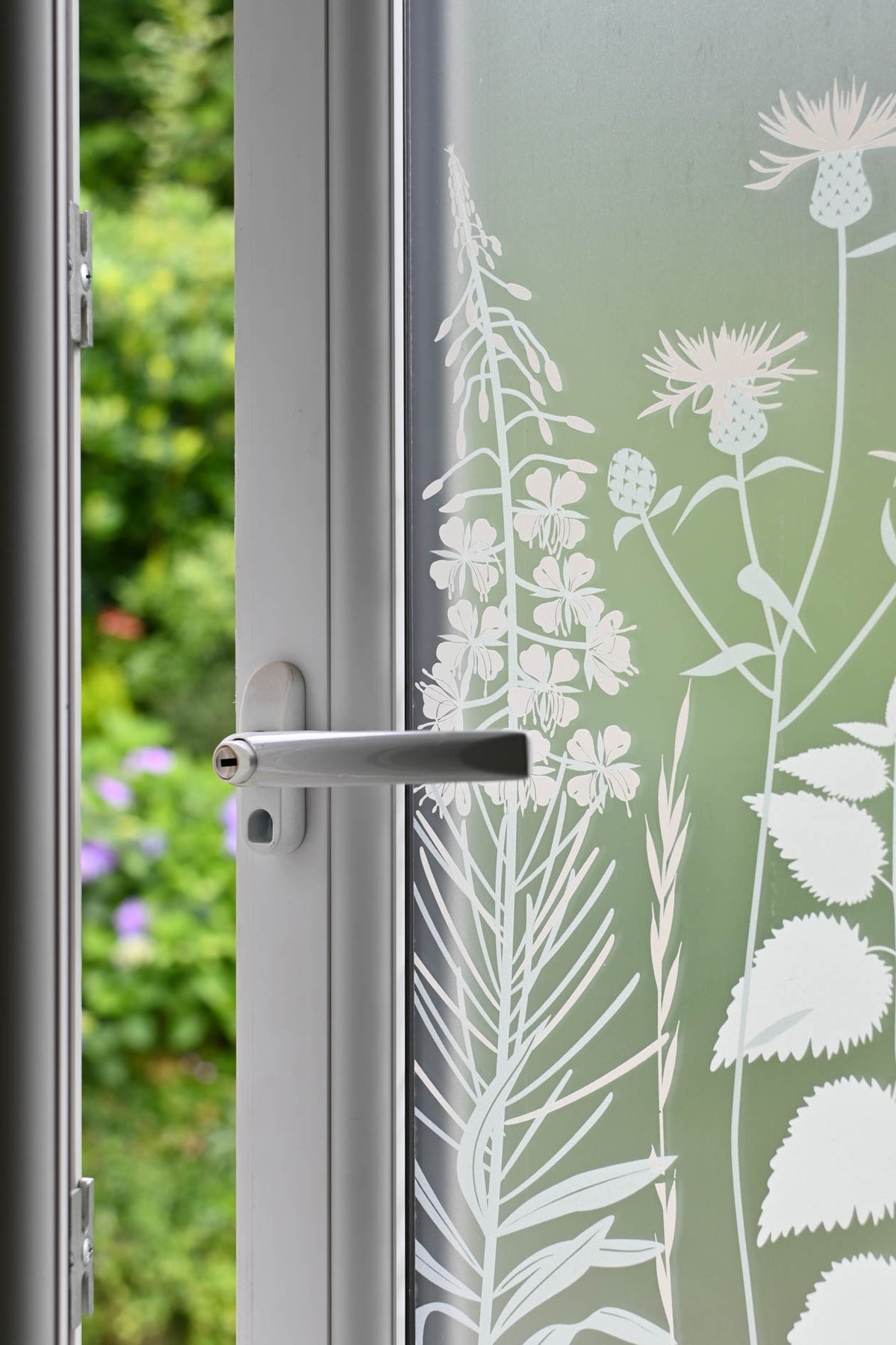 White printed frosted window film with nature inspired design applied to an open window, garden greenery is visible through the open part of the window.