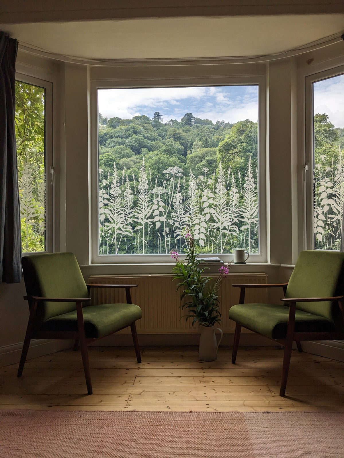 Nature inspired frosted pattern on a window film which has been applied to a large bay window in a living room setting.