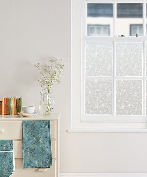 Room in a modern home with white walls and a window with white window frames; the glass has Helen Russell window film applied to it, featuring a repeated butterfly design. 