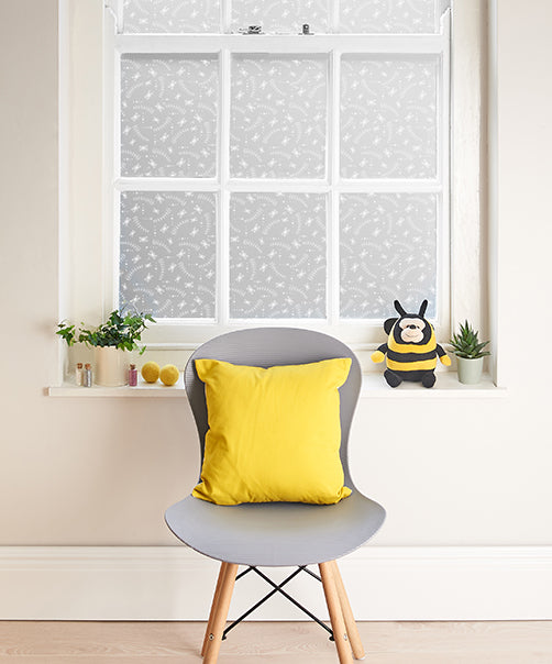 Internal view of a living space with a large window split into multiple panes, each pane has printed Helen Russell window film applied, and there is a grey chair with a yellow cushion in the foreground. 