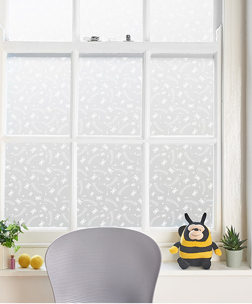 Window with Helen Russell decorative window film applied, grey chair, and plush bee toy on the windowsill. 