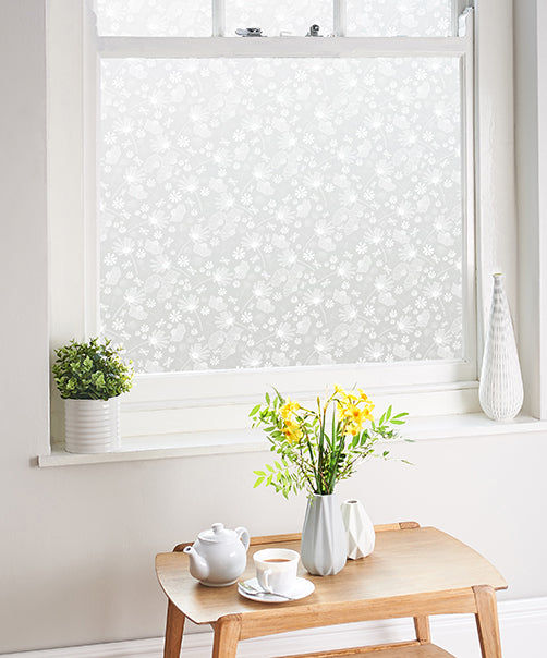 Window with decorative Helen Russell window film, wooden table with tea set and flowers, and plant on windowsill